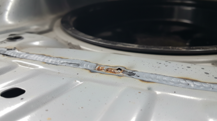 Two Winters Later Rust at the Weld Edge No Cracks Yet Trunk floor weld seam with faint surface rust and lifted seam sealer corner after two winters